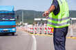 © wellphoto - Highway traffic police officer wearing a reflective vest signals a blue truck to stop at a checkpoint during daytime road inspection