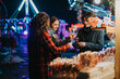 © qunica.com - A group of friends enjoying lollipops at a colorful outdoor evening fair with winter decorations, exuding warmth, joy, and friendship.