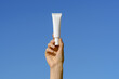 © Daryna  - Female hand holding white mockup tube of cream or serum on blue sky background. Concept of eye care cosmetics, beauty and aesthetics products