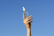 © Daryna  - Female hand holding transparent glass mock-up tube of facial serum on blue sky background. Concept of cosmetic products for moisturizing, nourishing and smoothing skin