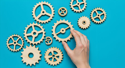 Poster - Hand Arranging Wooden Gears on Blue Background Representing Mechanical Design Concepts and Precision Engineering with Scattered Gears Overhead