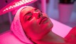 © Igor_Tichonow - A woman lies with eyes closed under pink LED light therapy, reflecting modern beauty treatments and skincare technology