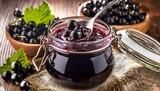closeup of stirring blackcurrant jam in a jar with fresh berries on rustic table