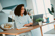 © deagreez - Smiling young woman working on laptop in modern home office interior during daylight hours