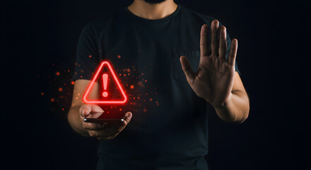 Poster - Man Holding Smartphone with Red Exclamation Triangle Against Dark Background in Studio Light with Hand Stop Gesture for Concept