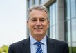 © Akheri - Portrait of a smiling mature man in a suit and tie standing in front of a modern building outdoors