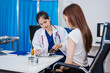 © NanSan - An Asian woman sits at a table consulting with a female doctor. They discuss her symptoms related to stress and depression. The doctor listens attentively and recommends treatment and medication