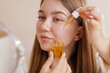 © st.kolesnikov - Young woman using cosmetic oil dropper for under-eye skincare treatment in beauty routine.