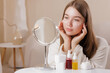 © st.kolesnikov - Girl with dotted face cream looking in mirror during morning facial care ritual.