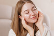 © st.kolesnikov - Smiling girl applying face cream dots, enjoying soft skincare ritual with closed eyes.