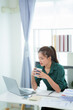 © PSG - Asian woman sitting at table with laptop and holding coffee cup