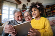 © NDABCREATIVITY - Happy senior couple using modern tech gadget tablet together with grandchild at home.