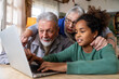 © NDABCREATIVITY - Joyful multiethnic grandparents with grandchild watching online game on laptop at home together