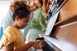 © NDABCREATIVITY - Happy man, pianist teacher giving piano lesson to a little school girl, playing music together