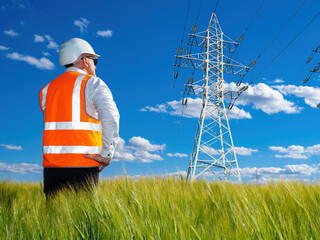 Poster - man is engineer at energy company. power line support under blue sky. electrical engineers in orange