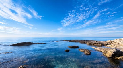 Fototapete - Serene coastal scene: clear blue water laps gently against sunlit rocks under a vibrant, cloud-streaked sky, offering a tranquil seascape. : Generative AI