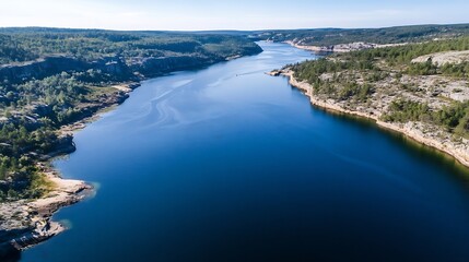Aufkleber - Aerial view of a serene river flowing through a rocky landscape, surrounded by lush green forests under a clear blue sky. The water is deep blue, reflecting the sunlight. : Generative AI