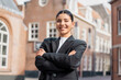 © Andrei - Confident young brunette realtor in sharp black suit posing with arms crossed outdoors, perfect for real estate marketing, career success, city professionalism, or personal branding