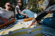 © qunica.com - Young friends enjoying a sunny picnic outdoors, playing board games and sipping coffee on a blanket. Their casual gathering showcases relaxation and leisure in a beautiful park setting.