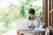 © Sumala - Asian woman digital nomad working remotely with laptop and phone outdoors smiling happily in natural bright environment