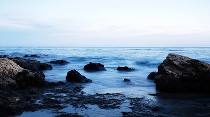 Poster - Serene coastal scene at twilight, featuring dark rocks partially submerged in calm, blue water under a pale sky.  The long exposure captures the gentle movement of the waves. : Generative AI