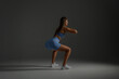 © Sandu - Young woman performing squats in a fitness studio with dim lighting and neutral background for strength training