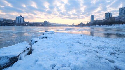 Aufkleber - Frozen riverbank cityscape at sunrise, snow covers rocks and ice, modern buildings and bridge in background, winter scene. : Generative AI