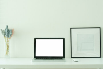 Laptop with a blank screen, coffee cup  and picture frame on white desk, for design mockups or editorial use.