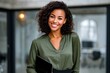 © Tanya - Confident young woman with curly hair in olive blouse stands ready for work, holding her tablet in a modern office space. Copy space.