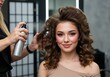© Manji - Stylist Spraying Woman's Hair in Salon with Curly Hairstyle