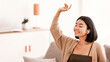© Prostock-studio - Enjoying Favorite Song. Portrait of happy asian female student wearing wireless earbuds listening to music, sitting on couch in living room with closed eyes and raising hand up. Positive lady resting