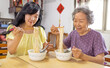 © Tom Wang - Happy senior mother and daughter eating noodles at home