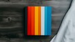© Gefo - A vibrant notepad with colorful stripes resting on a dark wooden surface beside a white cloth, perfect for creative inspiration and organization