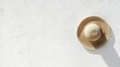 © Anastasia - Straw hat hanging on a white wall. the hat is round and has a wide brim with a spiral design on the front.