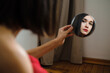 © Cavan Images - Woman admires reflection in small mirror indoors