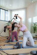 © Phimwilai - Two women are performing pilates exercises using reformer beds and resistance bands in a modern, bright gym, focusing on core strength and flexibility