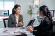 © Wasana - Two women are sitting at a desk, talking to each other