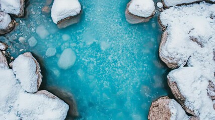 Poster - Winter landscape revealing turquoise water streaming between snow dusted rocky terrain, displaying contrasting cold white surfaces and vivid blue currents