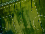 Aerial view of a youth soccer training session on a green field with long shadows cast by players in the late afternoon sun