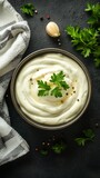 Creamy white sauce in a rustic ceramic bowl, garnished with fresh parsley leaves and black pepper, set against a dark textured background with kitchen towel and herbs