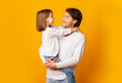 © Prostock-studio - Cheerful father and little daughter posing together on yellow background, dad holding girl, looking at each other