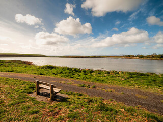 Wall Mural - one wooden old bench by a walking path with stunning view on open space with lake and amazing blue c