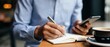 © Gpeg26 - A businessman writing notes in a notebook while checking his smartphone
