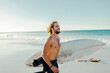 © Marko Geber - Young male surfer walking on a sandy beach while carrying his surfboard