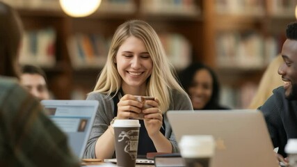 Poster - A group of college students are studying together in a library. They are drinking coffee, using laptops, and laughing. The background is filled with books and warm lighting.