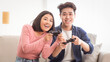 © Prostock-studio - Cheerful Asian Couple Playing Video Game Together Having Fun Sitting On Couch At Home. Videogames For Family Of Two, Computer Gaming Hobby And Domestic Weekend Leisure Concept