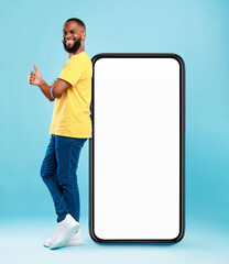 Poster - Funky black guy leaning on giant cellphone, showing thumb up gesture, recommending new mobile app or cool website, mockup for your ad design. Blue studio background