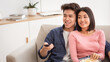© Prostock-studio - Chinese Family Couple Watching TV Together And Eating Popcorn On Weekend, Switching Television Channels With Remote Control Sitting On Couch In Living Room At Home.