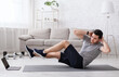 © Prostock-studio - Sport and healthy lifestyle. Man put hands behind his head and does exercises for abdominal muscles and watch online training at home in interior