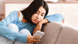 © Prostock-studio - Depression Concept. Portrait of frustrated asian young woman looking at smartphone, checking social media, lying on the couch. Upset lady waiting for his message or call, reading bad news